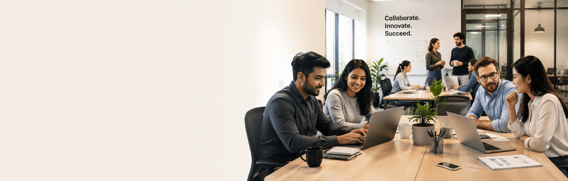 A team working at laptops in an office with a “Collaborate. Innovate. Succeed.” wall graphic